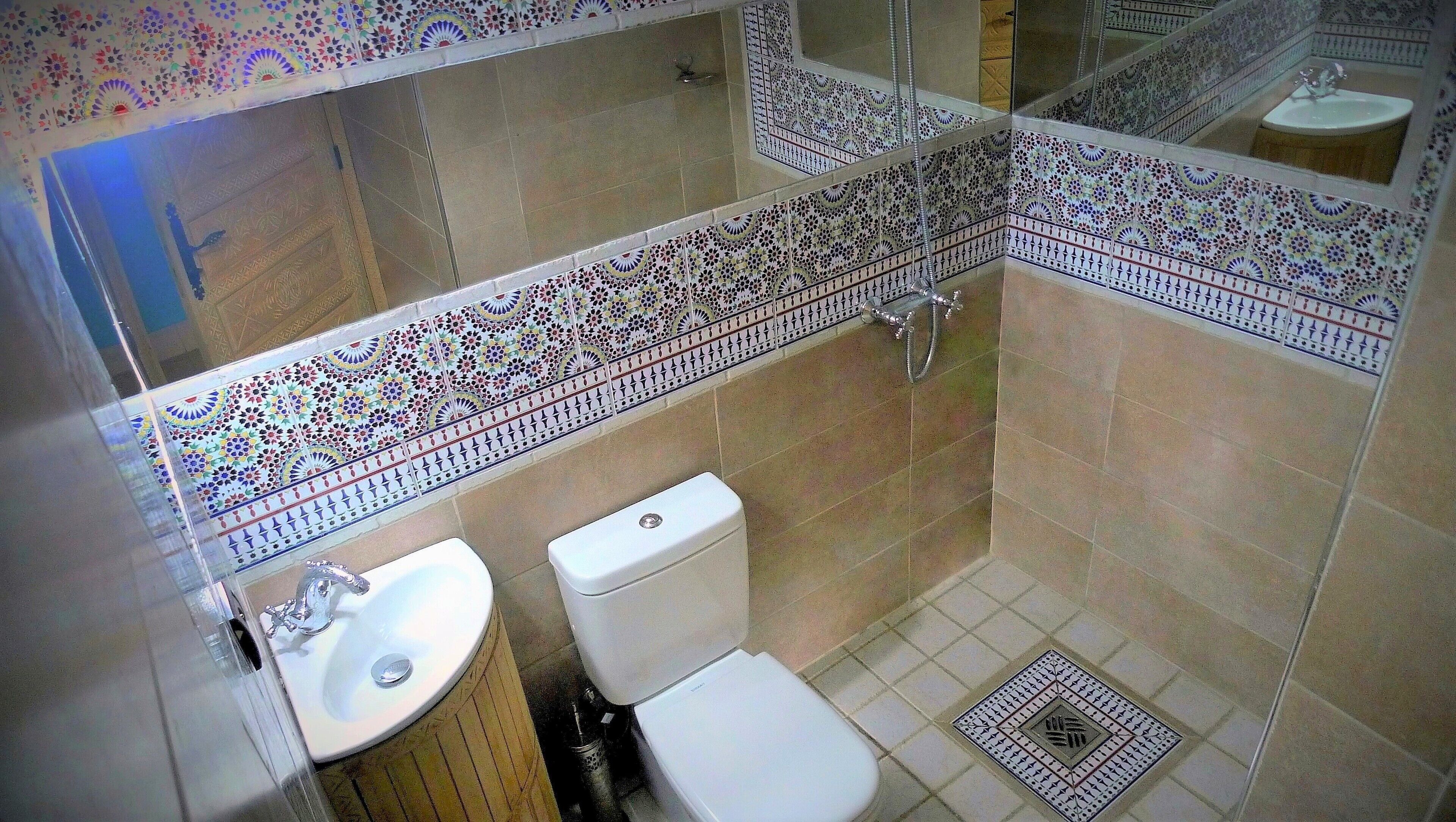 Un baño con inodoro, lavamanos y ducha. Las paredes están cubiertas de azulejos con un diseño decorativo.