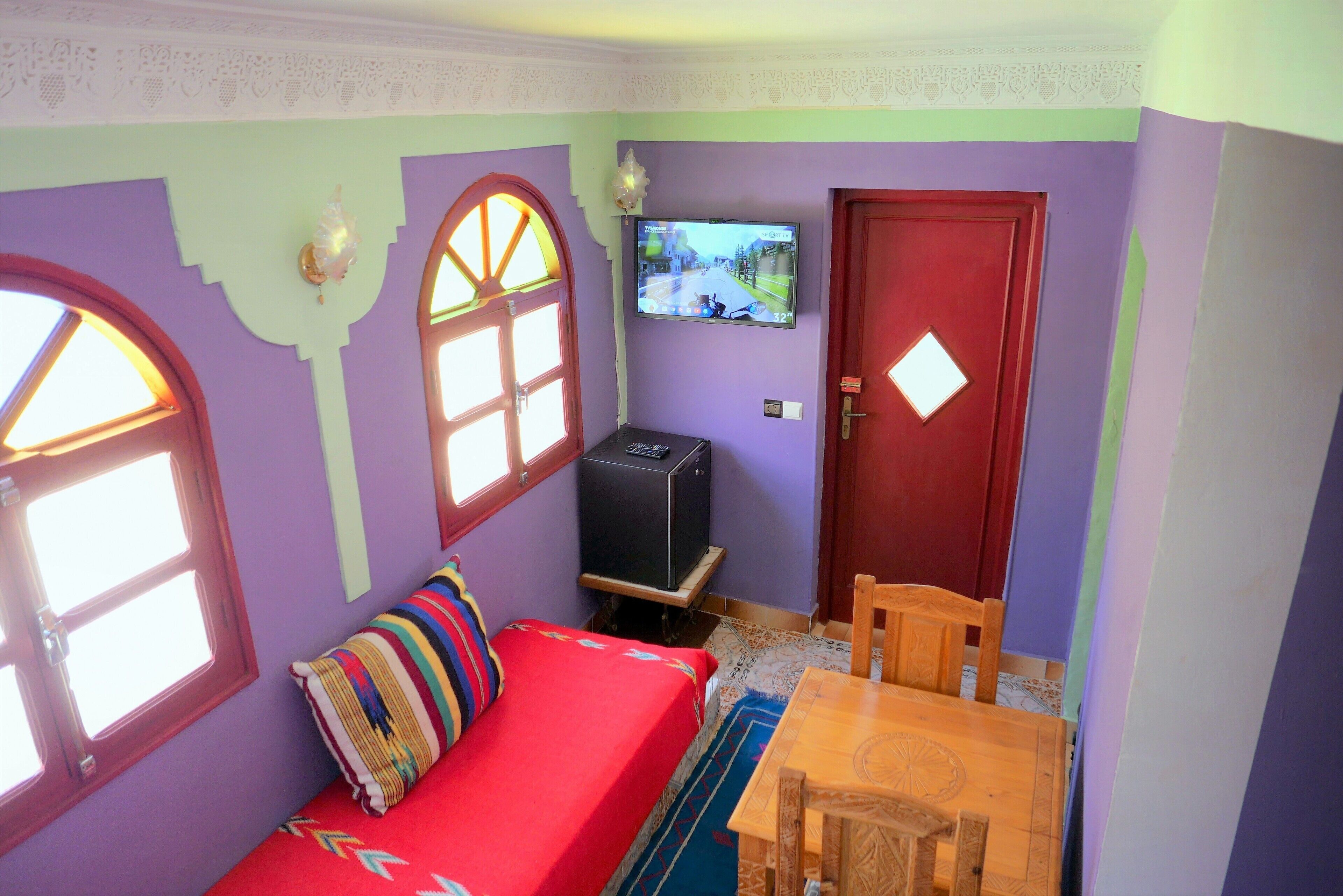 A small room with a bed, a TV, a wooden table, and a door.