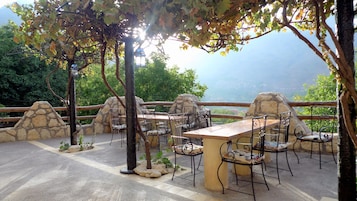 An outdoor patio with stone walls, metal chairs, and tables, overlooking a scenic landscape.