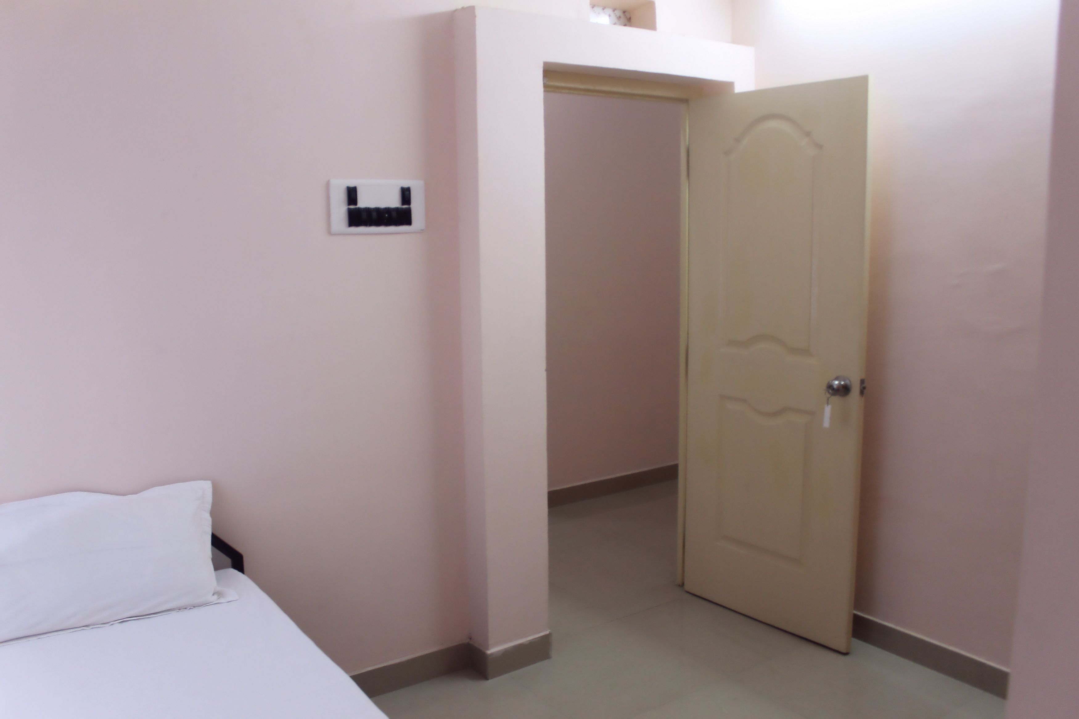 A bedroom with a bed, a door, and a light switch on the wall.