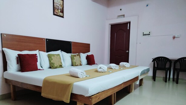 Habitación de hotel con una cama grande, cabecera de madera y un banco al pie de la cama. Hay dos sillas contra la pared y una puerta con pomo.