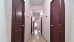 Un pasillo largo y estrecho con dos grandes puertas de madera a cada lado, que dan a las habitaciones. Las paredes están pintadas de un color claro y el suelo está cubierto de baldosas.