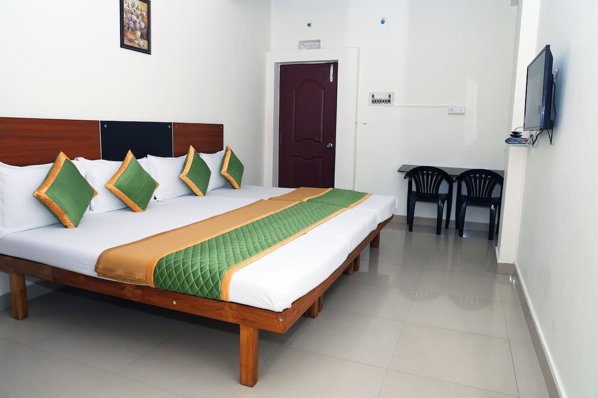 Une chambre d’hôtel bien aménagée, avec un grand lit, une tête de lit en bois, un téléviseur fixé au mur et une petite table avec deux chaises.