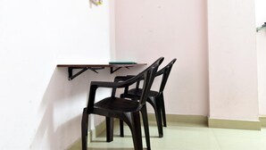 Una habitación pequeña con una pared blanca, una pared rosa y un piso blanco. Hay una mesa con superficie verde y una silla negra.