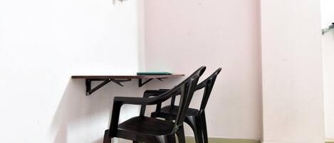 Una habitación pequeña con una pared blanca, una pared rosa y un piso blanco. Hay una mesa con superficie verde y una silla negra.