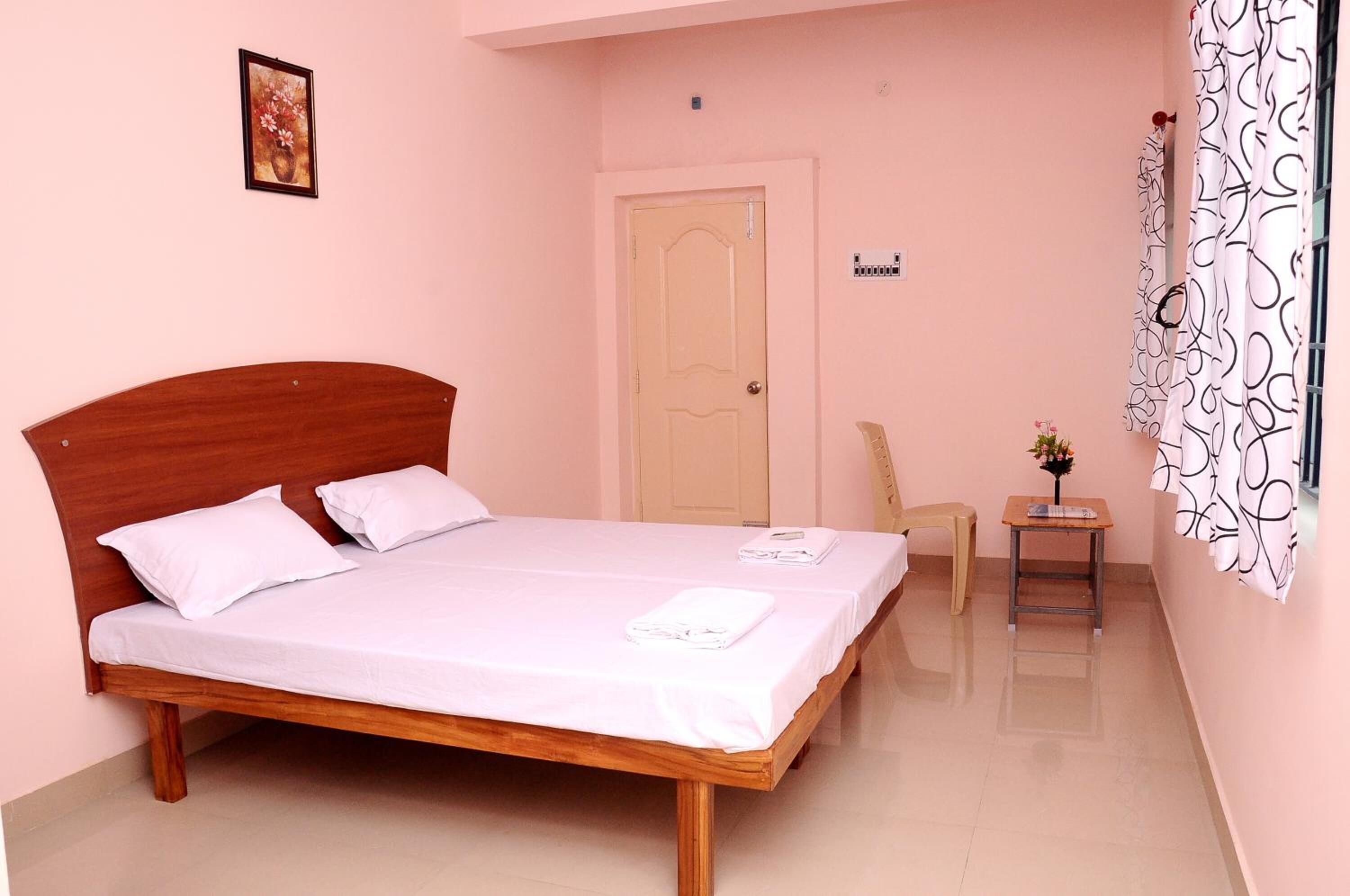 Un dormitorio con una cama de madera, una mesita con un florero, una silla y una puerta.