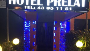 Ingresso di un hotel con insegna illuminata che riporta 'HOTEL PRELAT' e un numero di telefono.