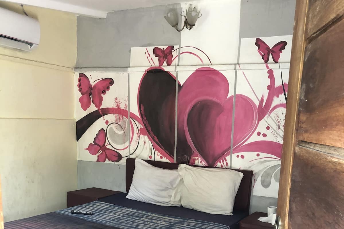 A room with a bed, a nightstand, and a wall with floral and heart designs.