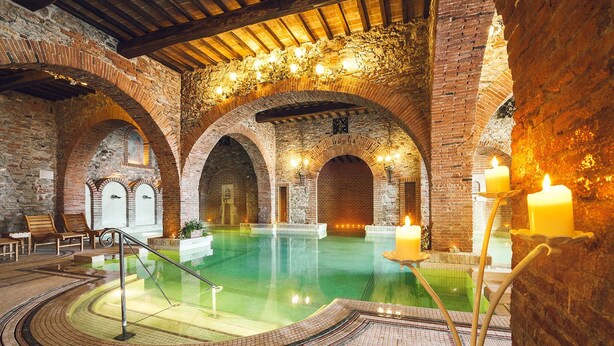 An indoor swimming pool with brick arches and a wooden ceiling, surrounded by seating and candles. - Casa Vacanze Dolce Vita (Campiglia Marittima)