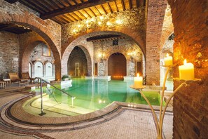 An indoor swimming pool with brick arches and a wooden ceiling, surrounded by seating and candles. - Casa Vacanze Dolce Vita (Campiglia Marittima)