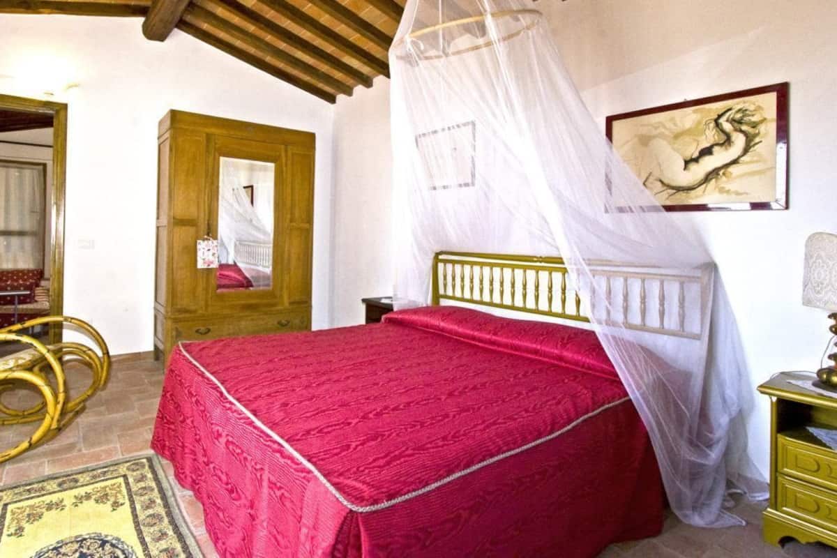A bedroom with a bed under a canopy, a wooden wardrobe, a chair, and a bedside table.