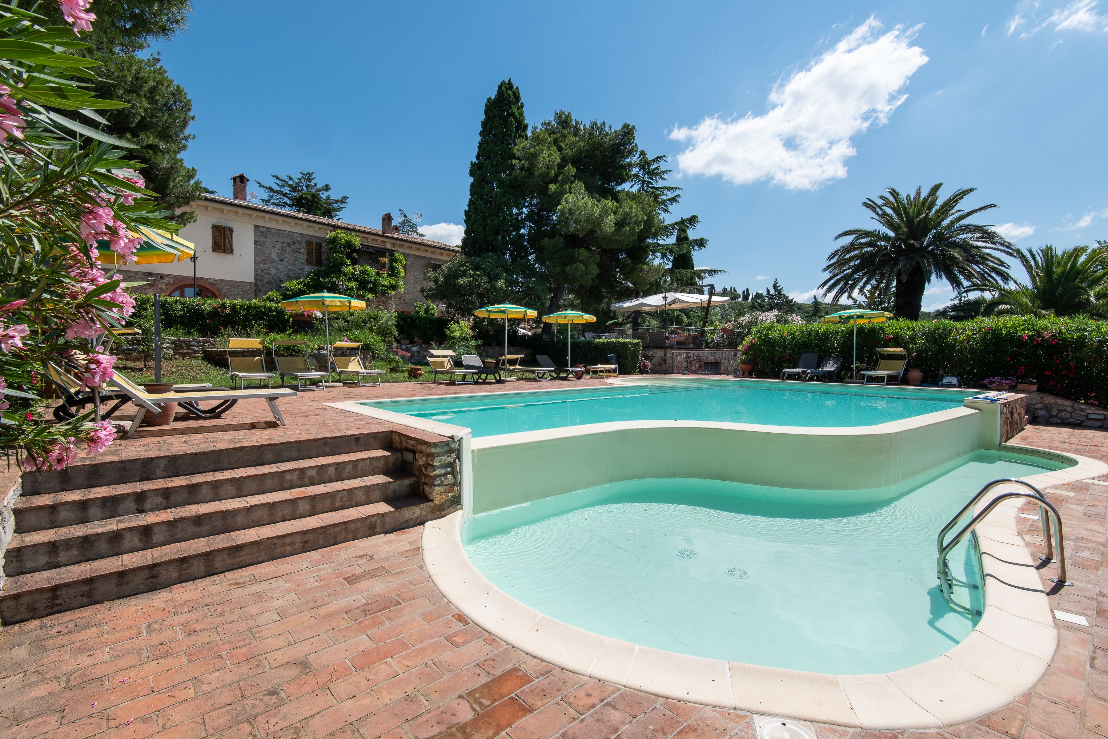 A swimming pool with a brick deck, surrounded by lounge chairs and umbrellas.