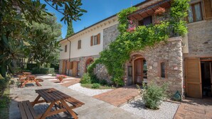 A courtyard with stone buildings, wooden tables, and potted plants. - Casa Vacanze Dolce Vita (Campiglia Marittima)