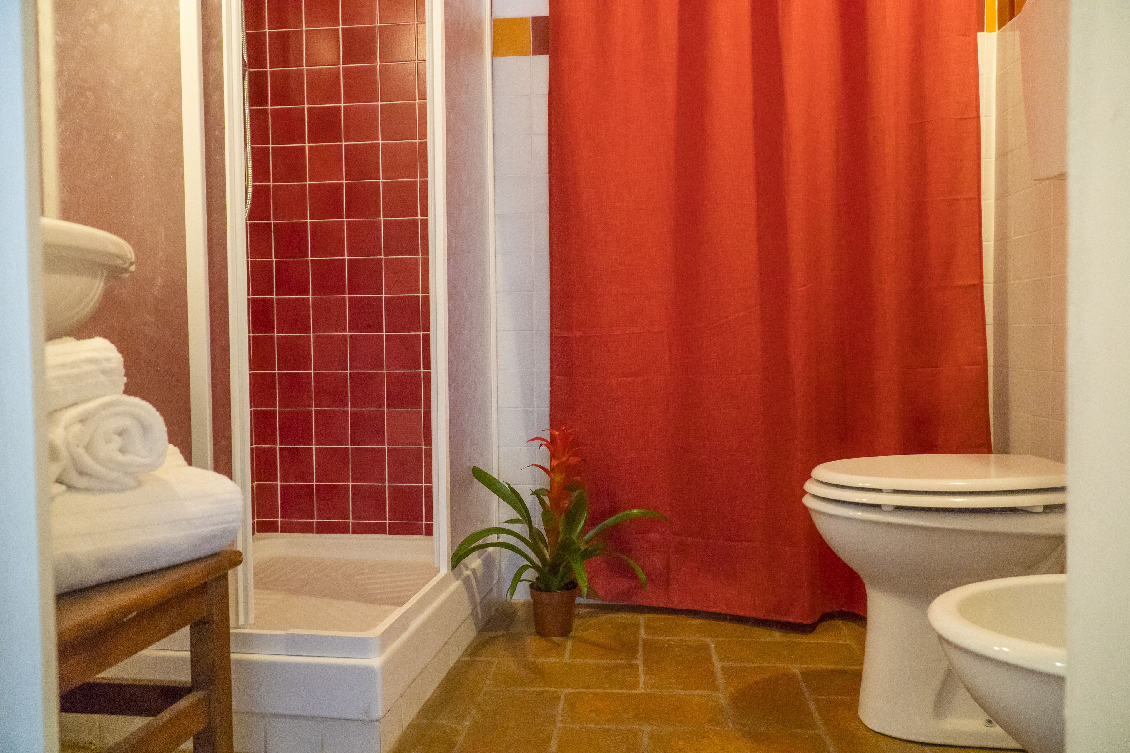 Un baño con inodoro blanco, cortina de ducha roja y una planta en maceta.