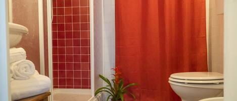 Un baño con inodoro blanco, cortina de ducha roja y una planta en maceta.