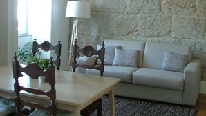 A living room with a stone wall, a sofa, a dining table with chairs, and hanging lamps. - Citybreak Apartments Bolhão (Porto)