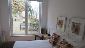 A bedroom with a large window, a bed with white bedding, two pillows with a wood grain pattern, a bedside table, and two framed pictures on the wall. - Citybreak Apartments Bolhão (Porto)