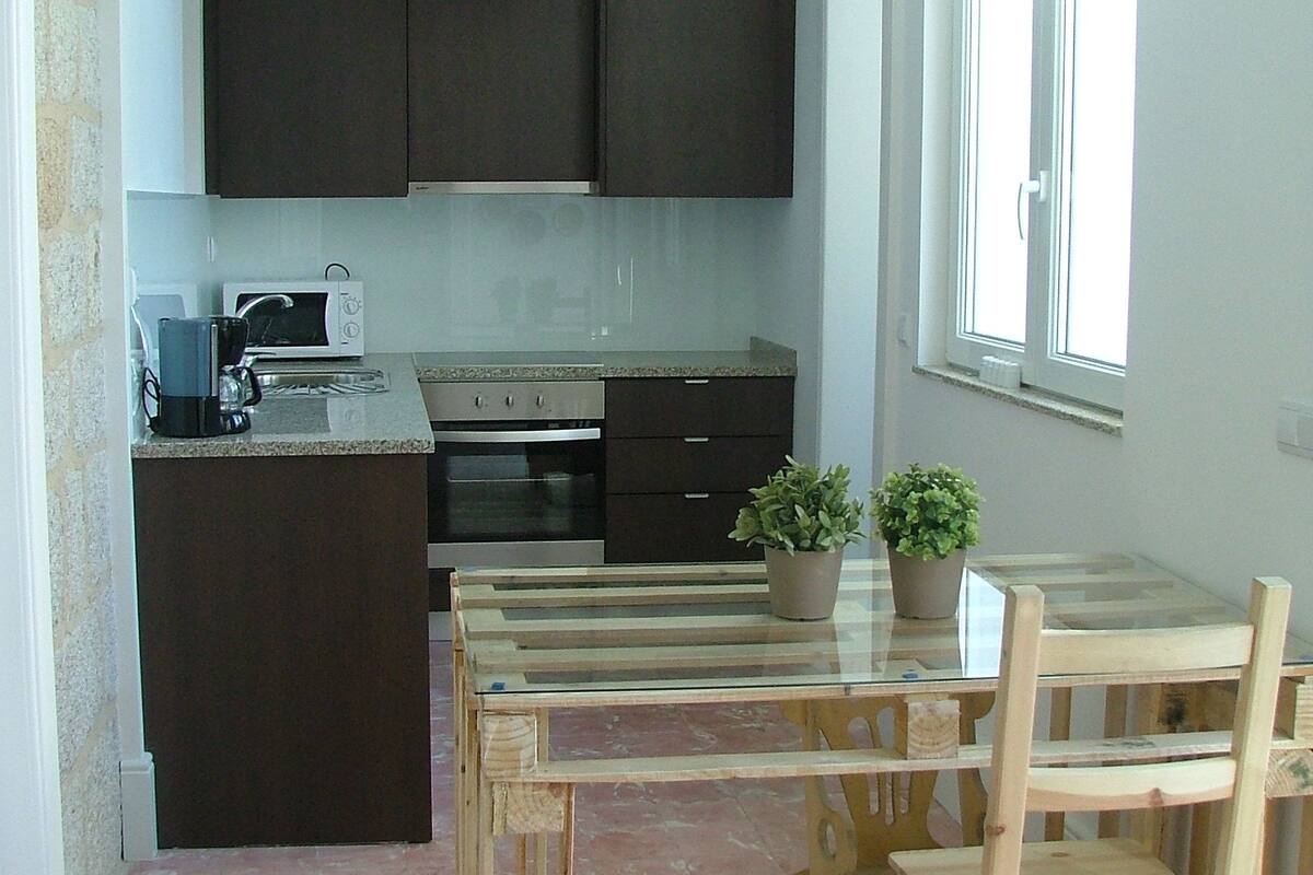 A kitchen with dark cabinets, a microwave, and a stove. There is a window with blinds, a table with chairs, and a potted plant.