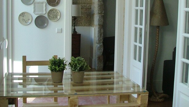 A dining area with a wooden table and chairs, a potted plant, and a wall-mounted plate collection. - Citybreak Apartments Bolhão (Porto)