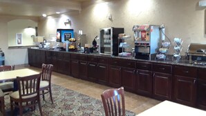 A hotel kitchen with a long counter, various appliances, and seating for guests. - Scottish Inns (Cresson)