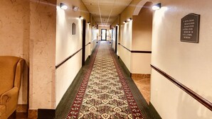 A hotel hallway with a patterned carpet, directional signs, and a ceiling with recessed lighting. - Scottish Inns (Cresson)