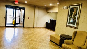A spacious lobby with a tiled floor, a reception desk, a framed picture on the wall, and an exit sign. - Scottish Inns (Cresson)