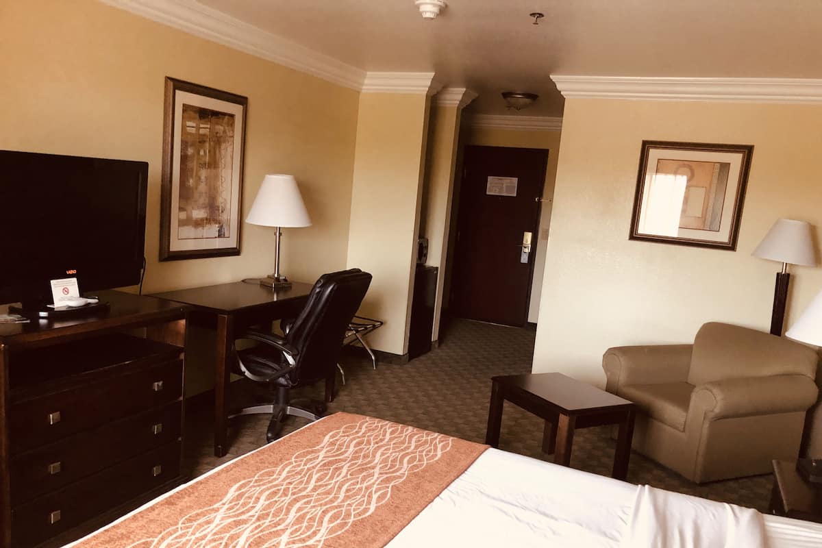 A hotel room with a bed, a desk, a chair, a television, and a door leading to another room.