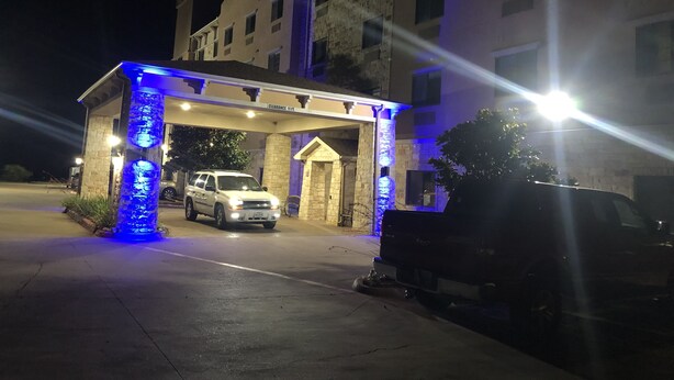 A hotel entrance with a covered driveway, a white SUV parked inside, and a black SUV parked outside. - Scottish Inns (Cresson)