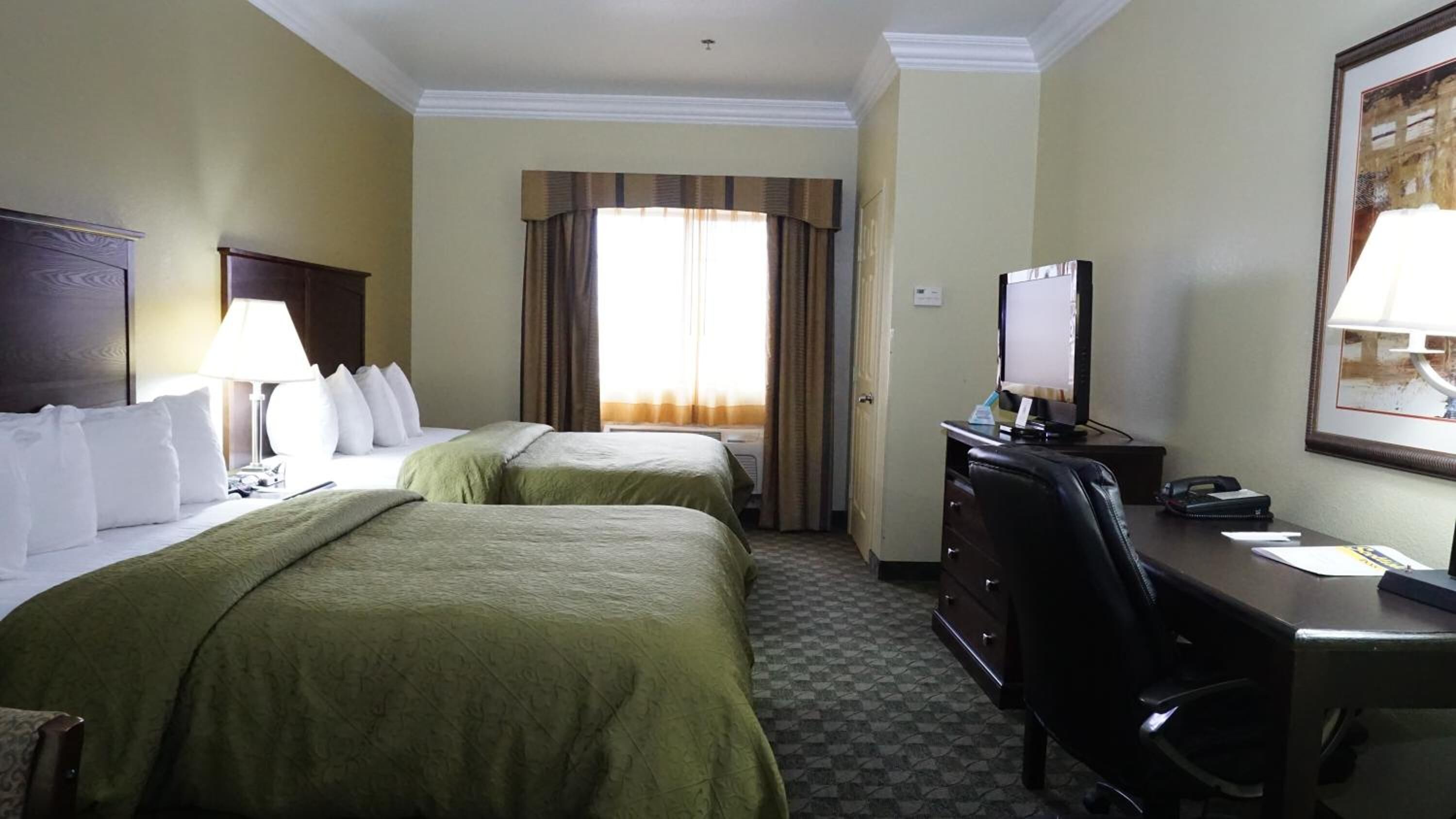 Une chambre d’hôtel avec deux lits, un bureau avec un ordinateur, une chaise et une fenêtre avec des rideaux.