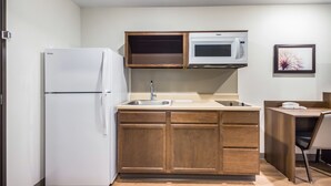 A compact kitchen with a refrigerator, microwave, sink, and wooden cabinets. - WoodSpring Suites Chicago Addison (Addison)