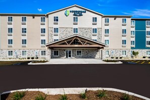 A hotel with a stone facade, a central entrance with a triangular roof, and a parking lot in front. - WoodSpring Suites Chicago Addison (Addison)