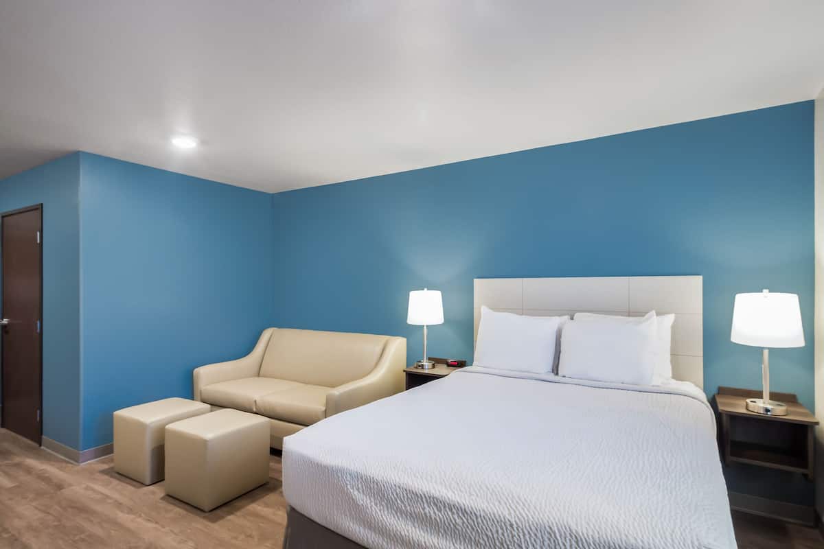 A hotel room with a large bed, two bedside lamps, a beige sofa, and a small table.