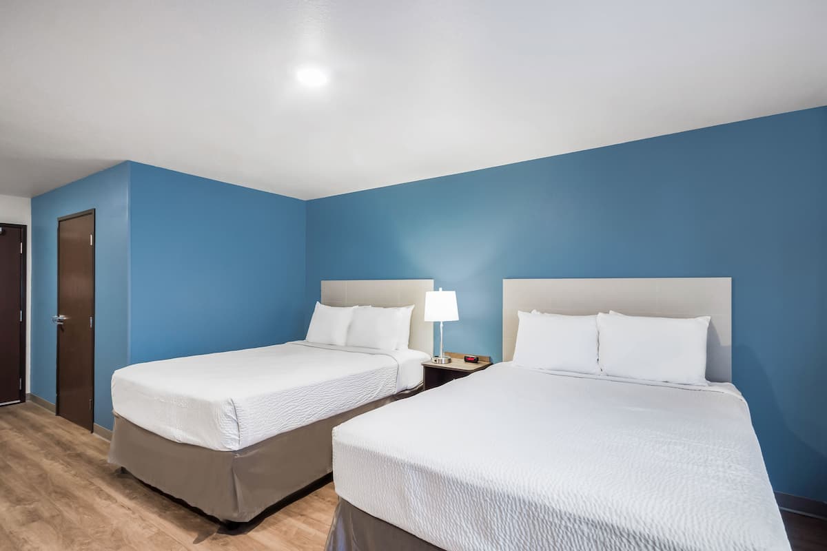 A hotel room with two beds, a nightstand, a lamp, and a door.