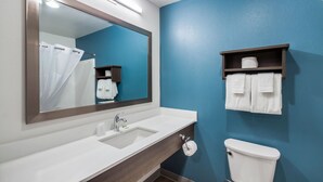 A bathroom with a white sink, a mirror, a blue wall, a toilet, and a towel rack. - WoodSpring Suites Chicago Addison (Addison)