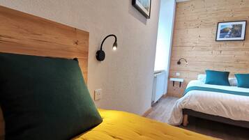 A hotel room with a wooden headboard, a green pillow, a yellow bedspread, a bedside table with a lamp, and a bed with white and teal bedding.