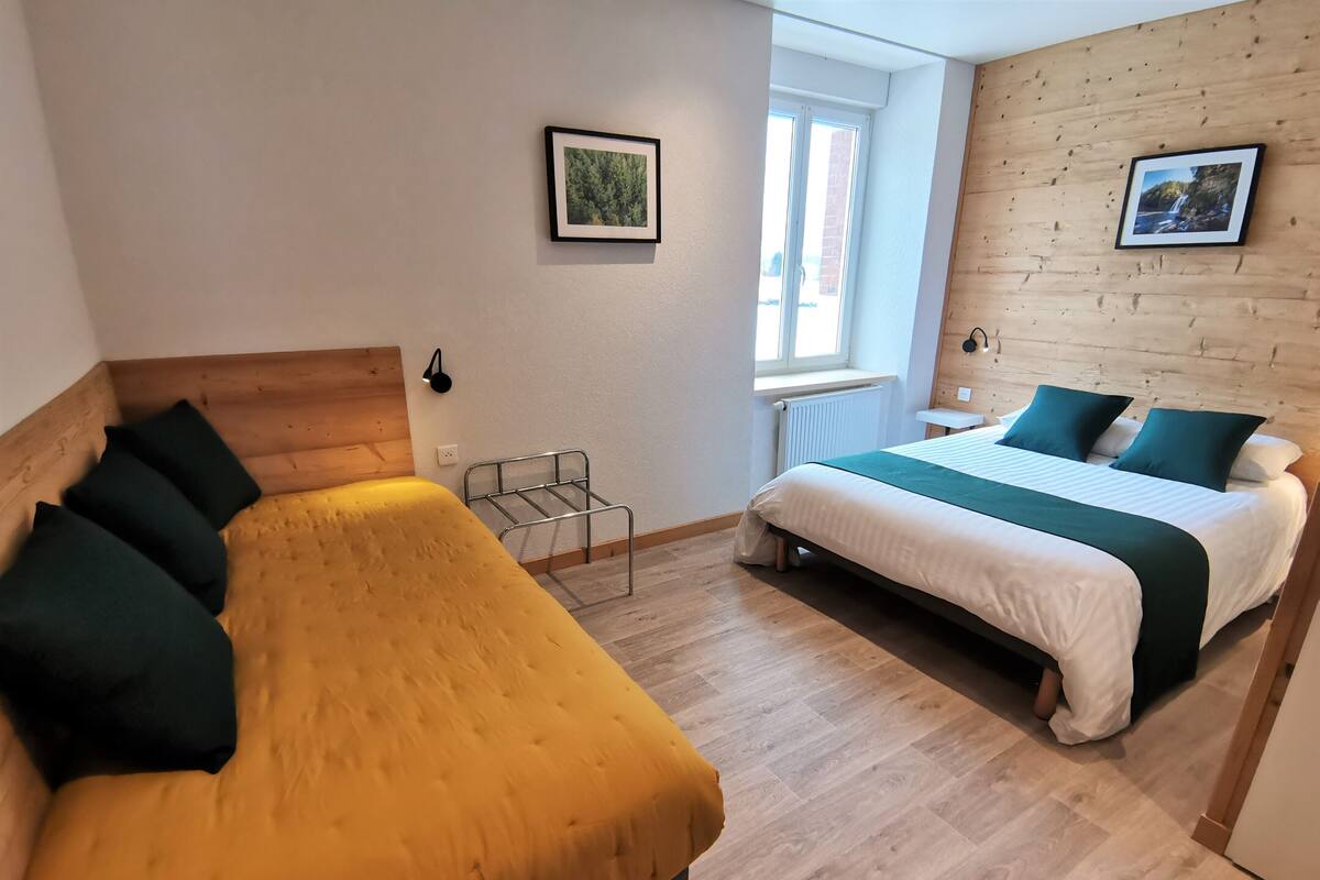 Une chambre avec deux lits, une tête de lit en bois, une fenêtre et un radiateur.