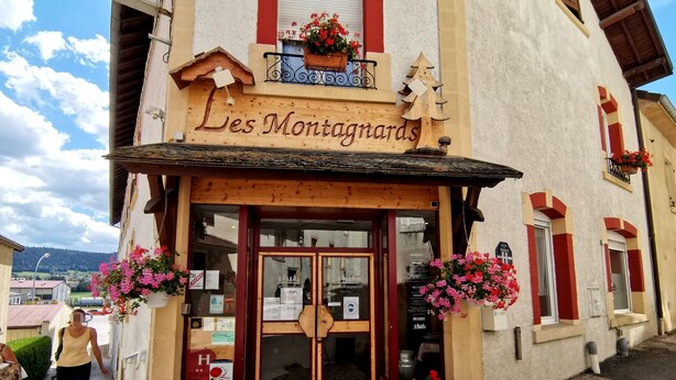Un hotel llamado "Les Montagnards" con fachada de madera, una entrada acogedora y arreglos florales.