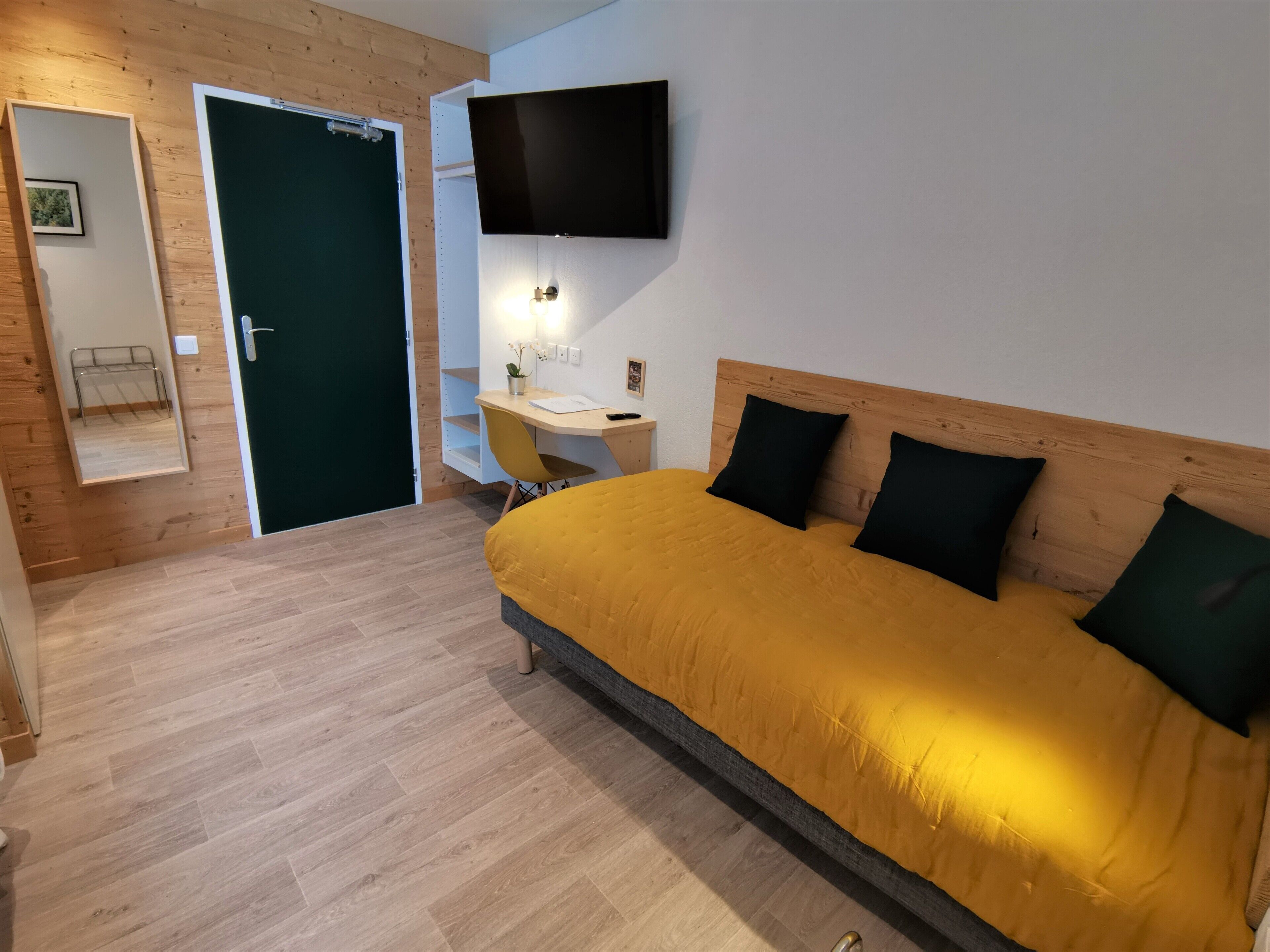 A bedroom with a bed, a desk, a chair, a TV, and a door.