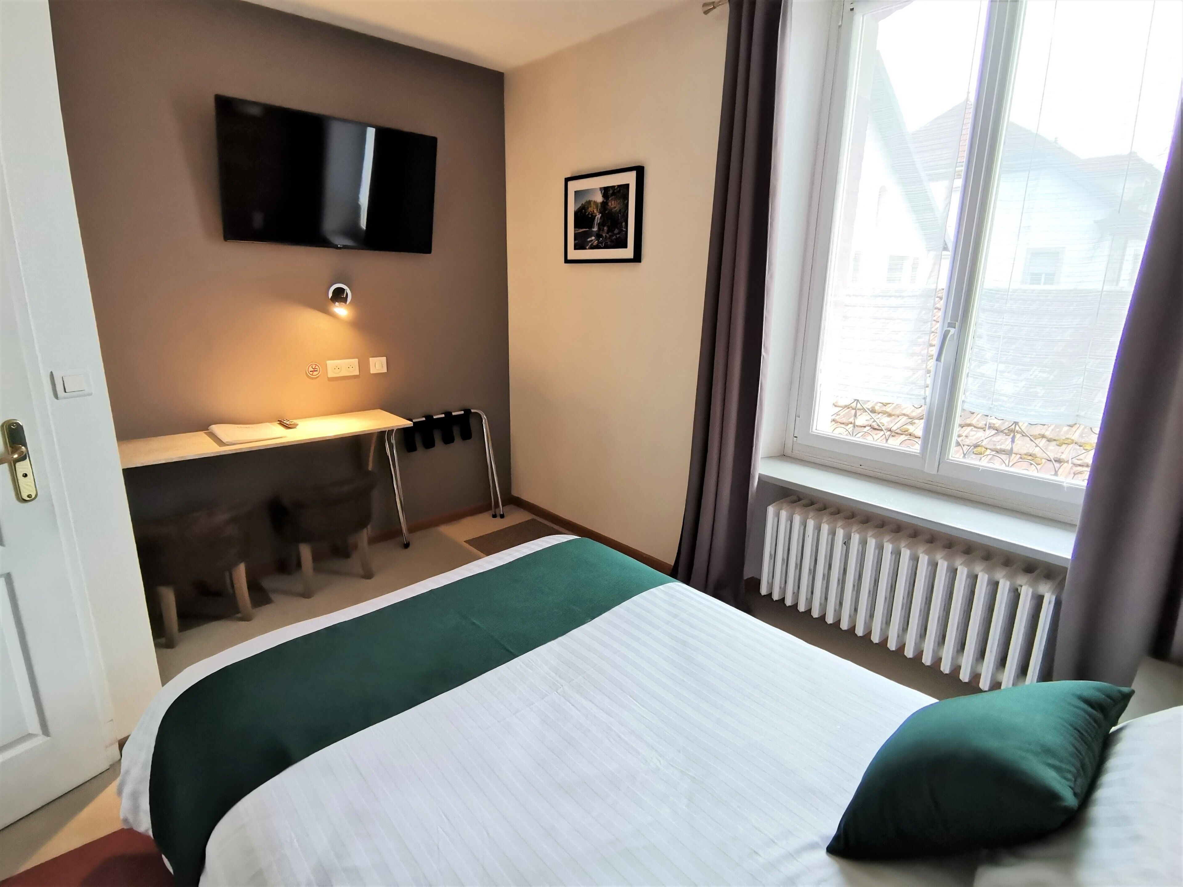 Ett hotellrum med en säng, ett skrivbord, en stol, en tv och ett fönster med gardiner.