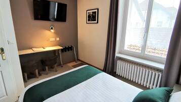 Ett hotellrum med en säng, ett skrivbord, en stol, en tv och ett fönster med gardiner.