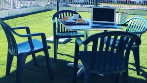 Una mesa con una laptop, un croissant y una taza en un espacio cubierto de césped con sillas.