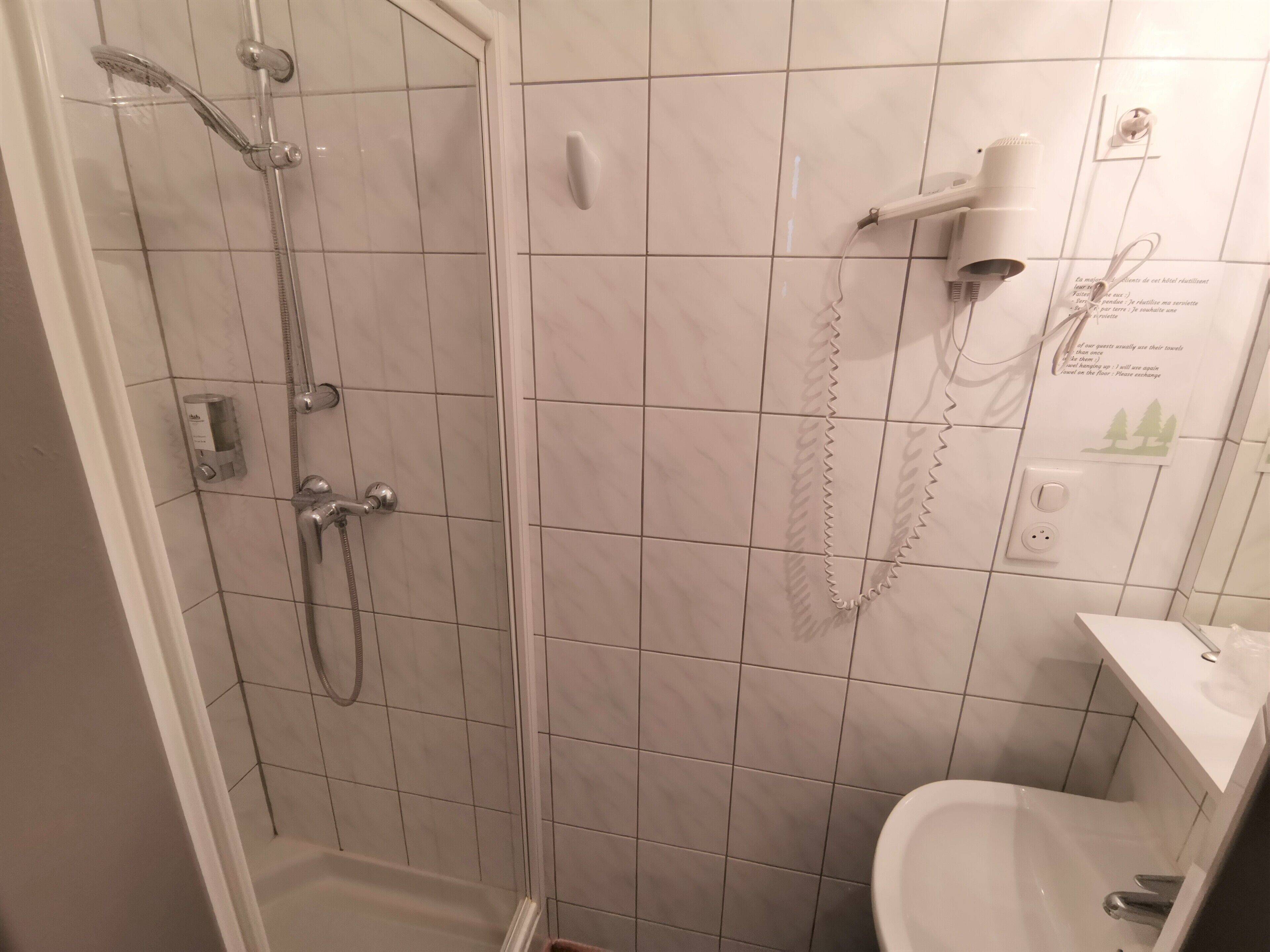 Un baño con ducha de vidrio, un lavamanos blanco y un secador de pelo montado en la pared.
