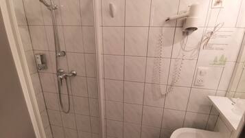 Un baño con ducha de vidrio, un lavamanos blanco y un secador de pelo montado en la pared.