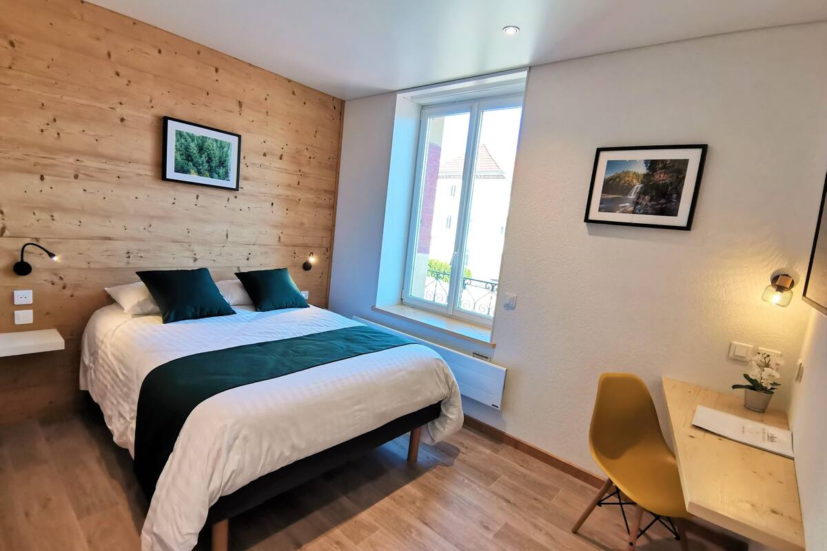 Une chambre à coucher comprenant un lit, un bureau, une chaise, une fenêtre et un tableau accroché au mur.