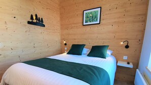 Una habitación con paneles de madera, una cama, una mesita de noche, un cuadro colgado en la pared y un estante con un control remoto.