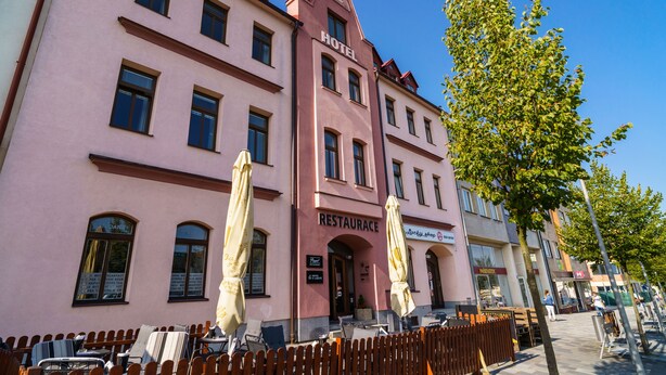 Um edifício rosa com um letreiro que diz "HOTEL RESTAURANCE" e área externa com mesas e guarda-sóis.