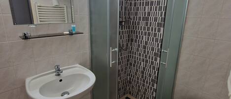 A bathroom with a glass-enclosed shower, a sink, and a small stool.