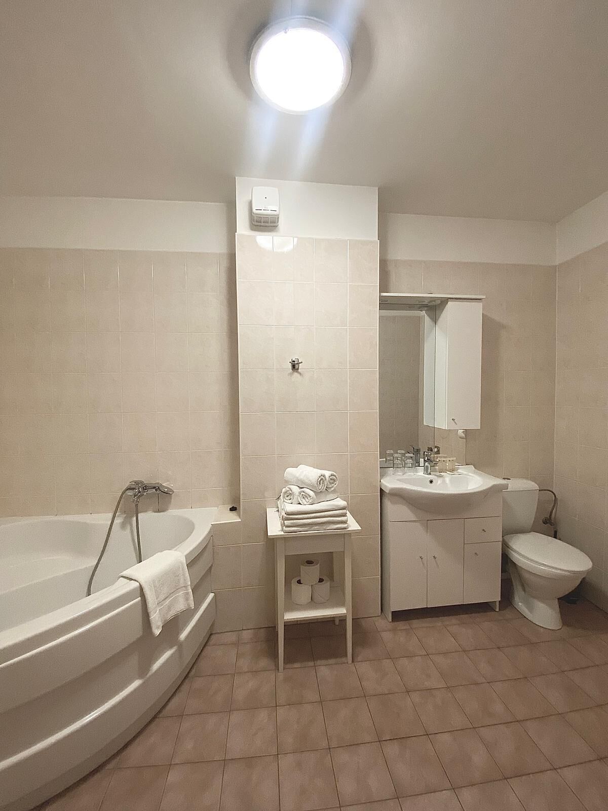 Ein Badezimmer mit Badewanne, Toilette, Waschbecken und einem kleinen Regal mit Handtüchern.