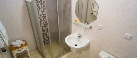 Un baño con cabina de ducha de vidrio, un lavabo, un inodoro y un taburete de madera pequeño con toallas.
