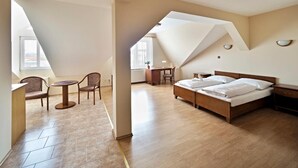 Quarto com cama de madeira, escrivaninha e cadeira, teto inclinado e janelas amplas.